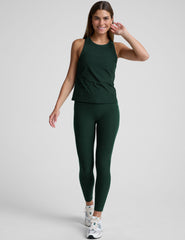 model is wearing a green tank top and green high-waisted midi length leggings with pockets on a plain background.