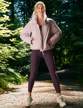 model wearing a pink puffer and purple high-waisted midi length leggings with pockets.