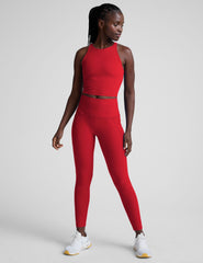 woman wearing a red cropped tank and high-waisted midi length pocket leggings on a plain background.