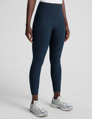 model is wearing blue high-waisted midi length leggings with side pockets on a light gray background.