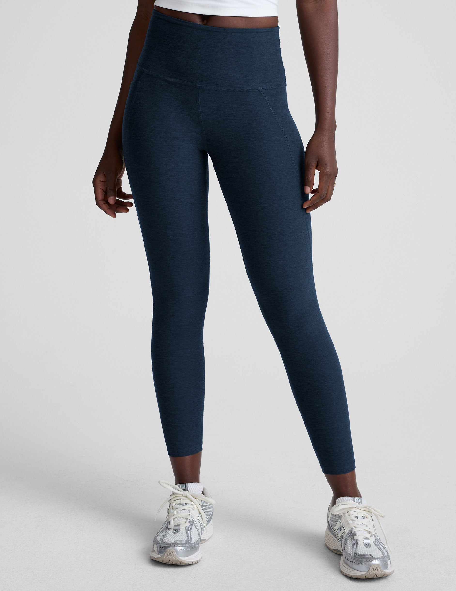 model is wearing blue high-waisted midi length leggings with side pockets on a light gray background.