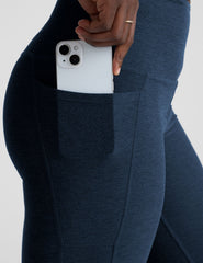 model wearing navy blue leggings with a pocket holding a white phone on a light gray background.