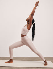 Woman in a yoga pose on a white mat with a plain background wearing a chai color set.