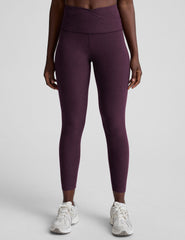 model wearing purple high-waisted midi length leggings with a front crossover detail on the waistband on a plain background.