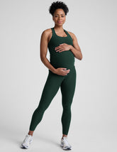 pregnant woman wearing a green tank top and leggings on a plain background.