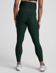 pregnant woman wearing green maternity leggings on a plain background.