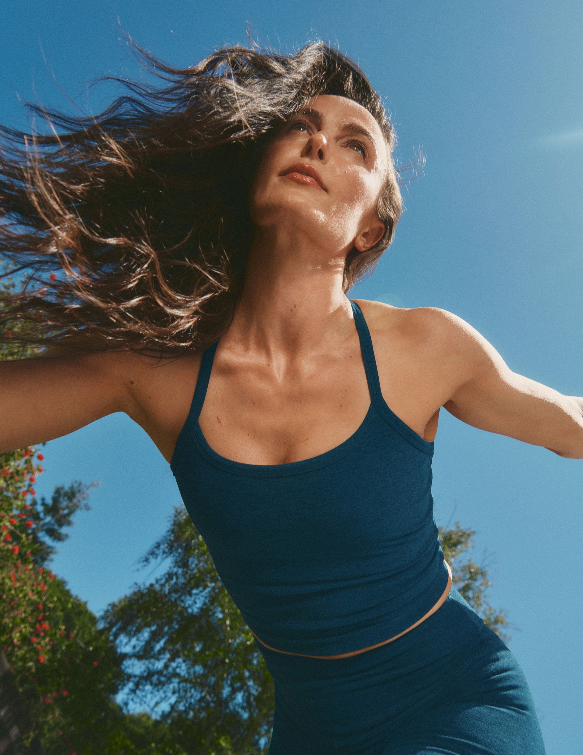 model in a blue racerback cropped tank and leggings with windblown hair against a clear blue sky.