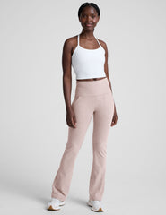woman wearing a white racerback cropped tank and pink pants against a plain background.