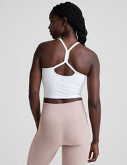 woman wearing a white racerback cropped tank and pink pants against a plain background.