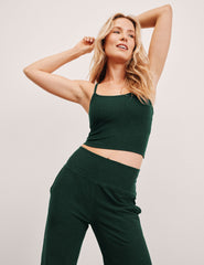 woman wearing a green racerback cropped tank top and pants against a plain background.