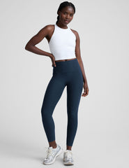 woman wearing a white high-neck racerback cropped tank and navy leggings on a plain background.