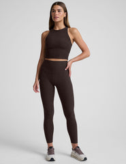 woman wearing a brown high neck racerback cropped tank and leggings on a plain background.