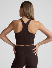 woman wearing a brown high neck racerback cropped tank and leggings on a plain background.