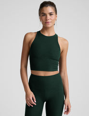 woman wearing a green high-neck racerback cropped tank and leggings on a plain background.