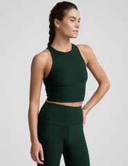 woman wearing a green high-neck racerback cropped tank and leggings on a plain background.