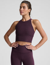 model wearing a purple high neck racerback cropped tank top and purple high-waisted midi length leggings against a plain background.