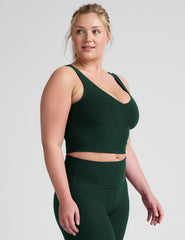 woman wearing a green soft v-neck cropped tank and joggers against a plaind background.
