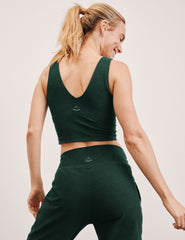 woman wearing a green soft v-neck cropped tank and joggers against a light background.