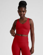 woman wearing a red v-neck cropped tank and leggings on a plain background.