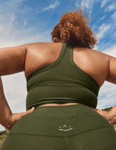 model wearing an olive green cropped racerback tank and leggings with a blue sky background.