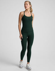 woman wearing a green tank top and leggings on a light gray background.