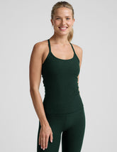 woman wearing a green tank top and leggings on a light gray background.