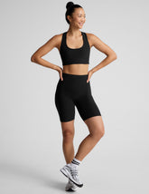 Woman wearing a black sports bra and biker shorts on a light gray background