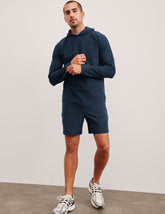 man wearing a navy blue hoodie and shorts set on a plain background.