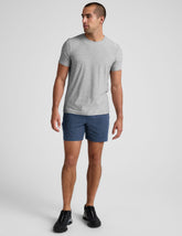 man wearing a grey t-shirt and blue shorts on a plain background.