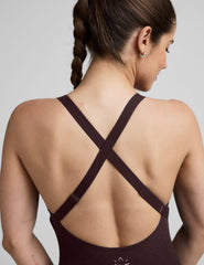 woman wearing a dark brown midi length jumpsuit on a plain background.