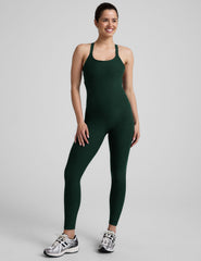 model wearing a green midi length tank jumpsuit with criss-cross back straps on a plain background.