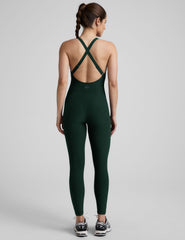 model wearing a green midi length tank jumpsuit with criss-cross back straps on a plain background.