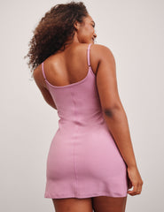 model is wearing a pink mini length dress with slim adjustable straps and built-in shorts with pockets.