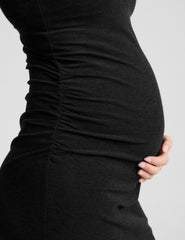 woman wearing a black maternity midi sleeveless dress on a plain background.