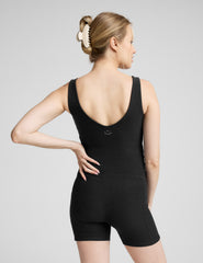 woman wearing a black maternity sleeveless jumpsuit on a plain background.