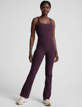 model wearing a purple square neck bootcut sleeveless jumpsuit on a plain background.