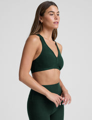 woman wearing a green sports bra and leggings on a light gray background.