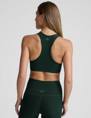 woman wearing a green sports bra and leggings on a light gray background.