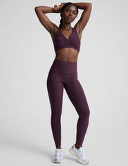 model wearing a purple soft v-neck racerback sports bra and leggings on a plain background.