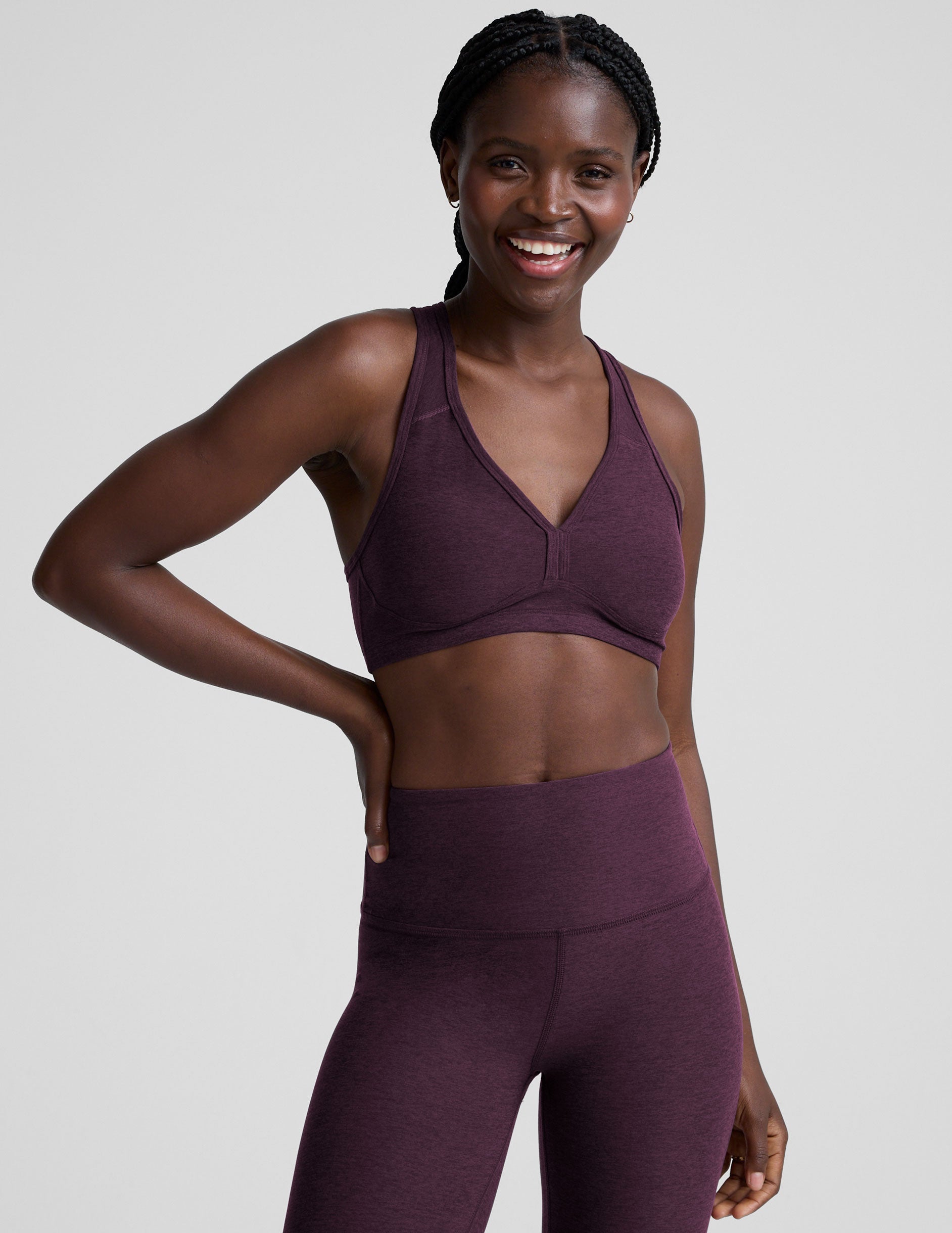 model wearing a purple soft v-neck racerback sports bra and leggings on a plain background.