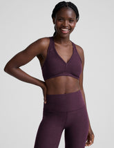 model wearing a purple soft v-neck racerback sports bra and leggings on a plain background.