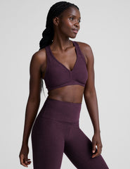 model wearing a purple soft v-neck racerback sports bra and leggings on a plain background.