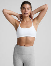 woman wearing a white slim racerback sports bra and gray leggings on a plain background.