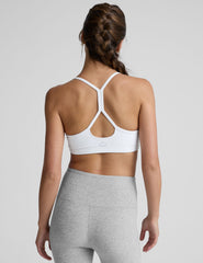 woman wearing a white slim racerback sports bra and gray leggings on a plain background.