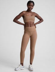 model wearing a brown slim strapped racerback bra and leggings on a light gray background.
