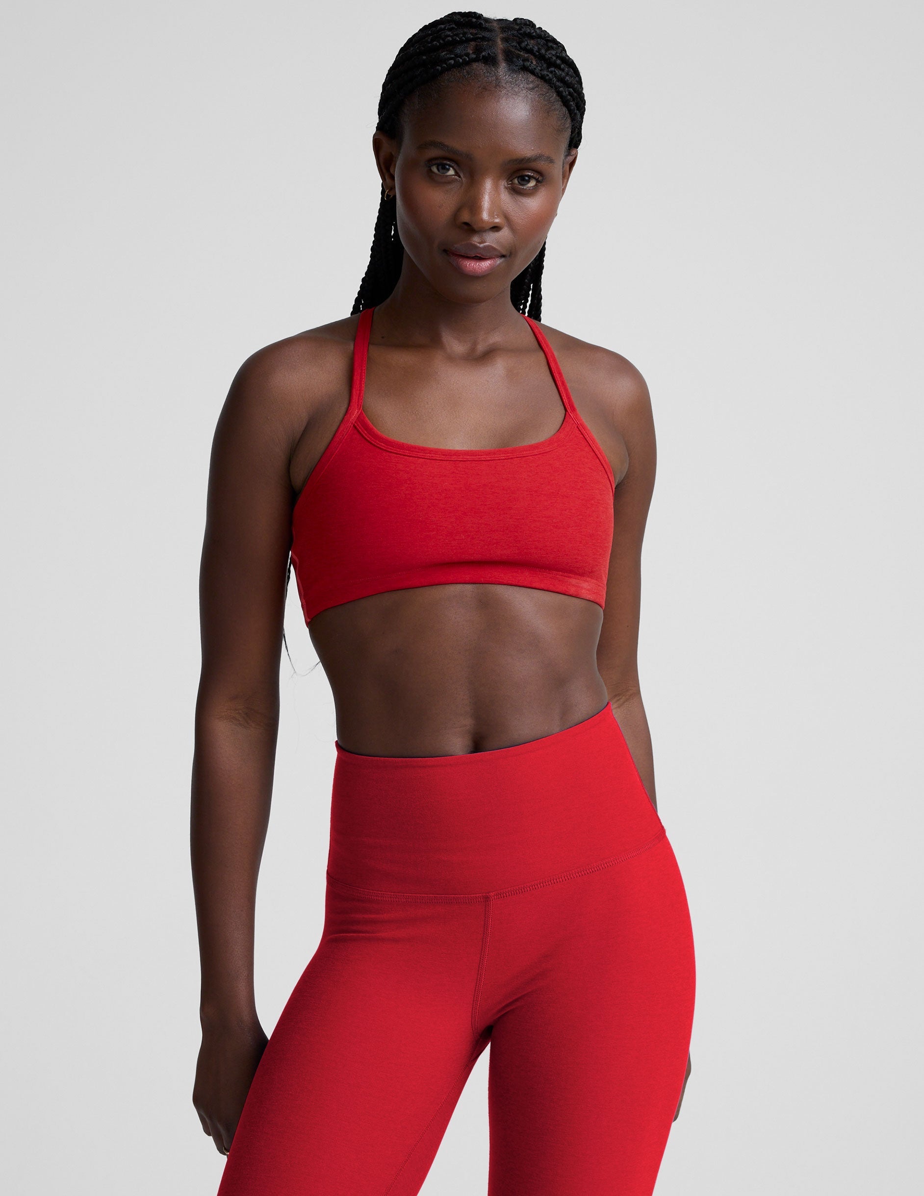 Woman wearing a red sports bra and leggings on a light background.
