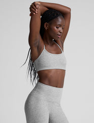 model is wearing a gray racerback bra with slim spaghetti straps and leggings against a plain background.