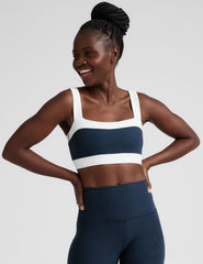 model is wearing a blue square neck bra with white horizontal colorblock stripe panels and a blue high-waisted midi length leggings.