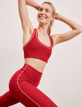 Woman wearing a red sports bra and leggings with white piping on a light background.