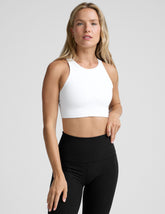 model wearing a white high-neck racerback sports bra and black leggings on a light gray background.